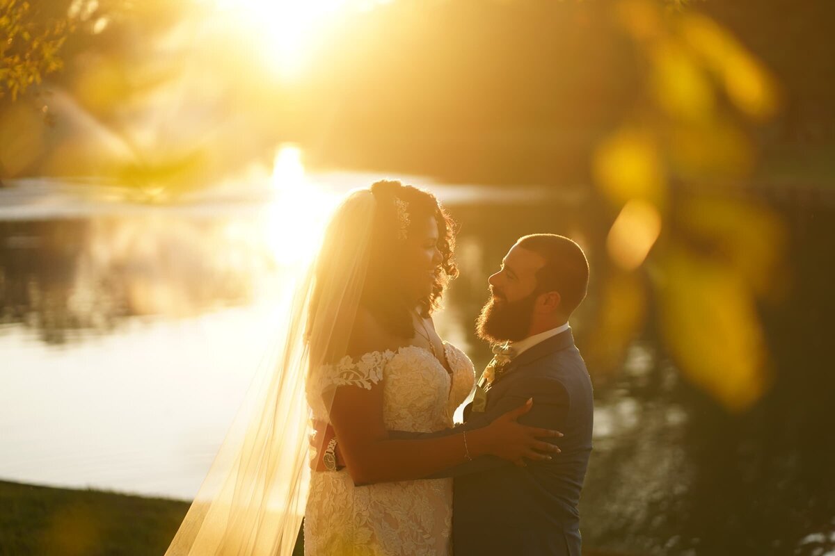 Wedding couple holding each other and smiling next to a lake.