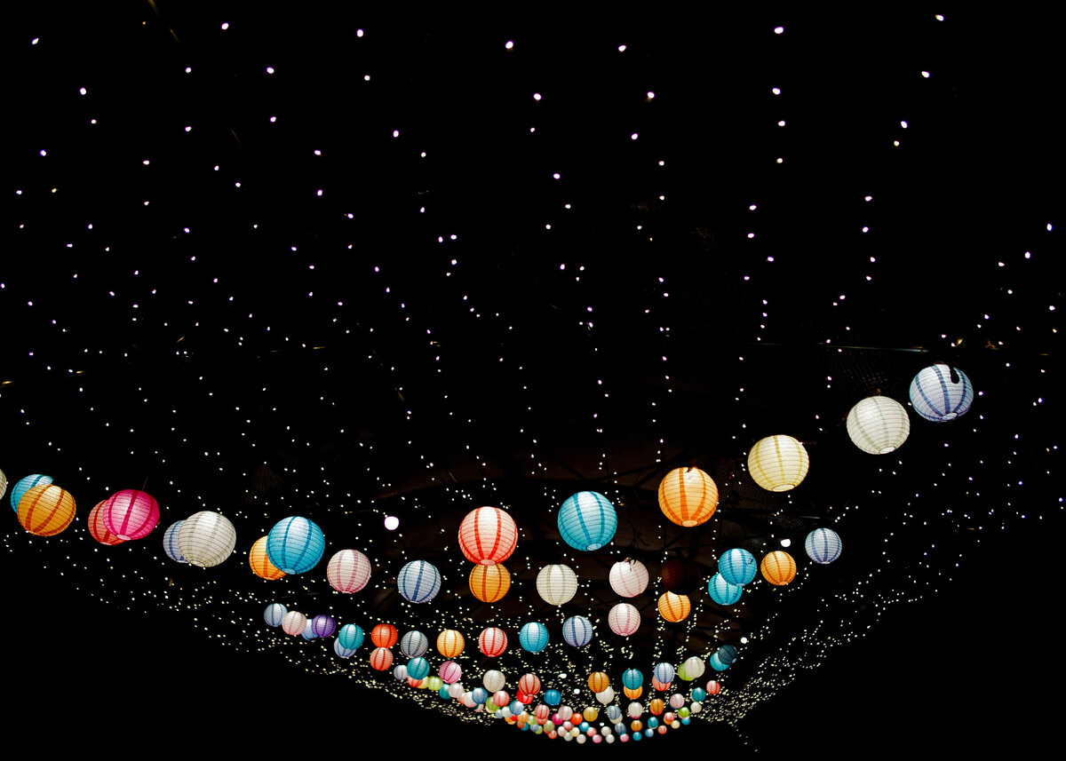 A colourful string of paper lanterns and fairy lights against the black night sky.