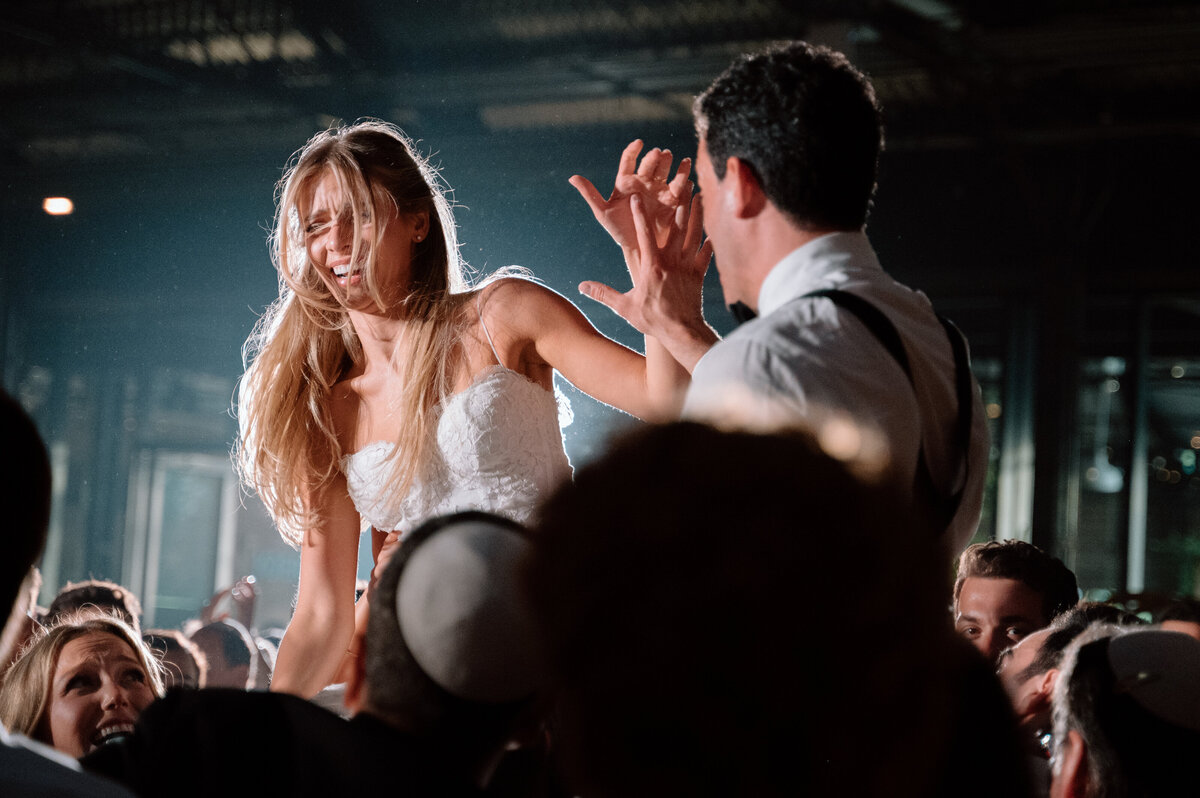 Bride and groom lifted simultaneously during hora with joyful expressions.