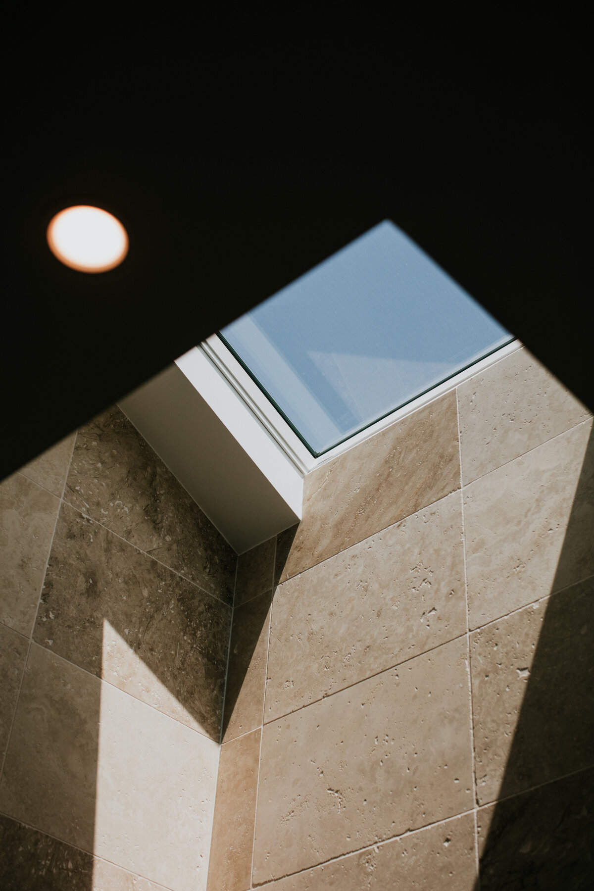 Sunlight from the skylight illuminates a tiled interior wall, complemented by a small round ceiling light nearby, showcasing the elegance of bespoke interior design Newcastle NSW offers.