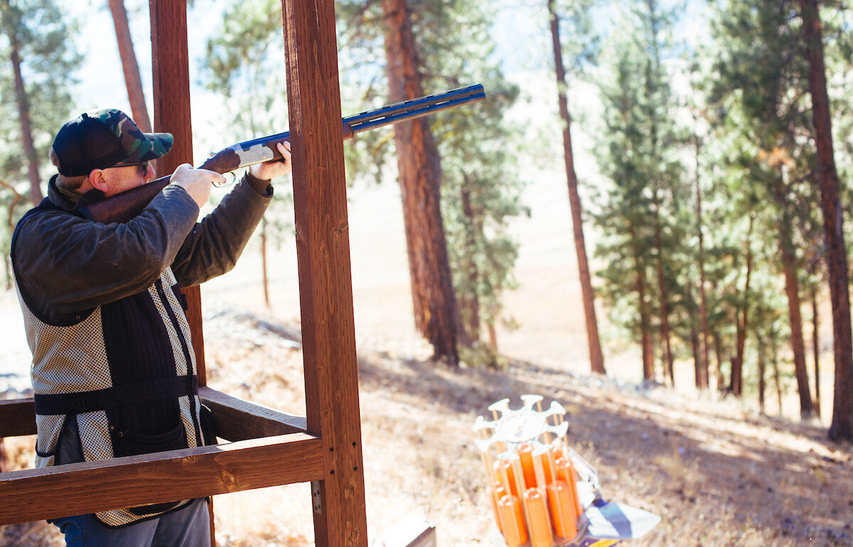 Man holding a riffle pointing it out towards the trees