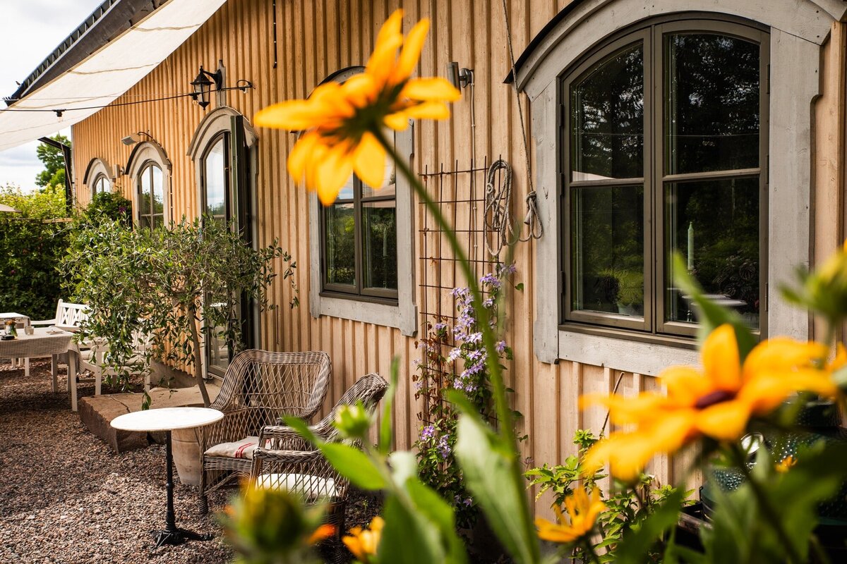 Trivsam uteplats vid pensionat med korgstolar och blommande växter – perfekt för sommarfika i trädgården.