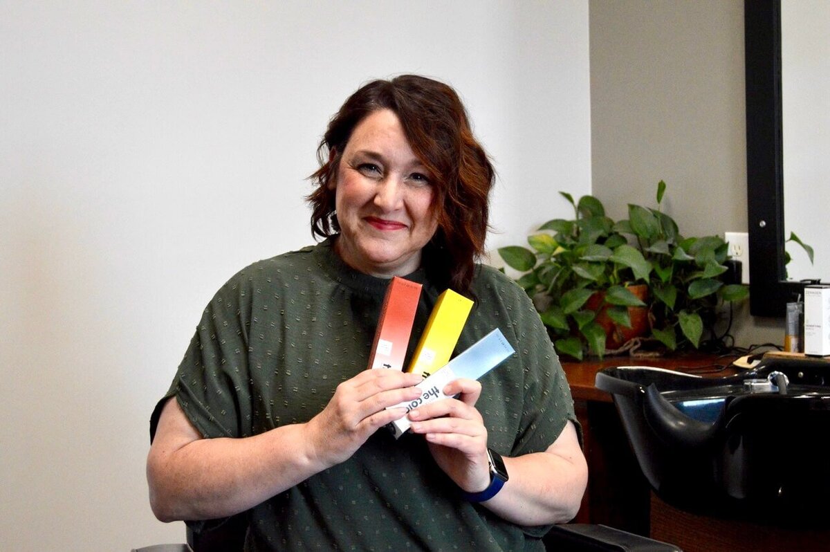 A smiling woman sitting in a salon chair, holding color swatches, showcasing the client satisfaction and personalized service at 212 Salon, Spa, & Barbershop.