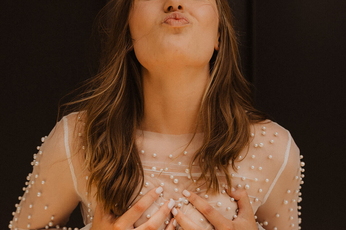 Woman wearing sheer pearl shirt clutches her breasts in boudoir photography session