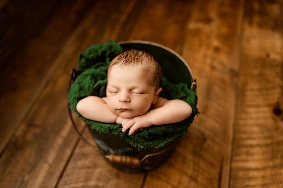 baby posed in green bucket asleep