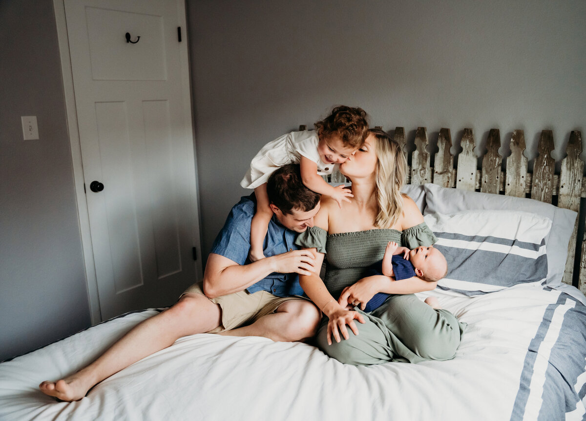 Newborn Photographer, mom holds baby and dad leans into her as their young daughter climbs on them