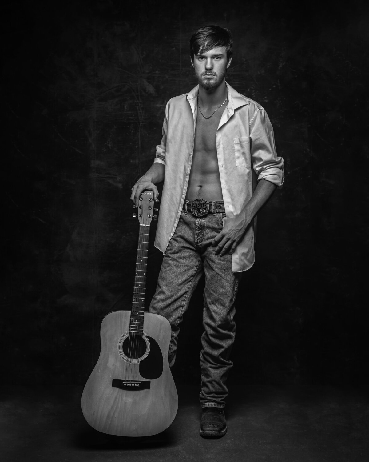 man with open shirt holding a standing guitar and standing in studio with