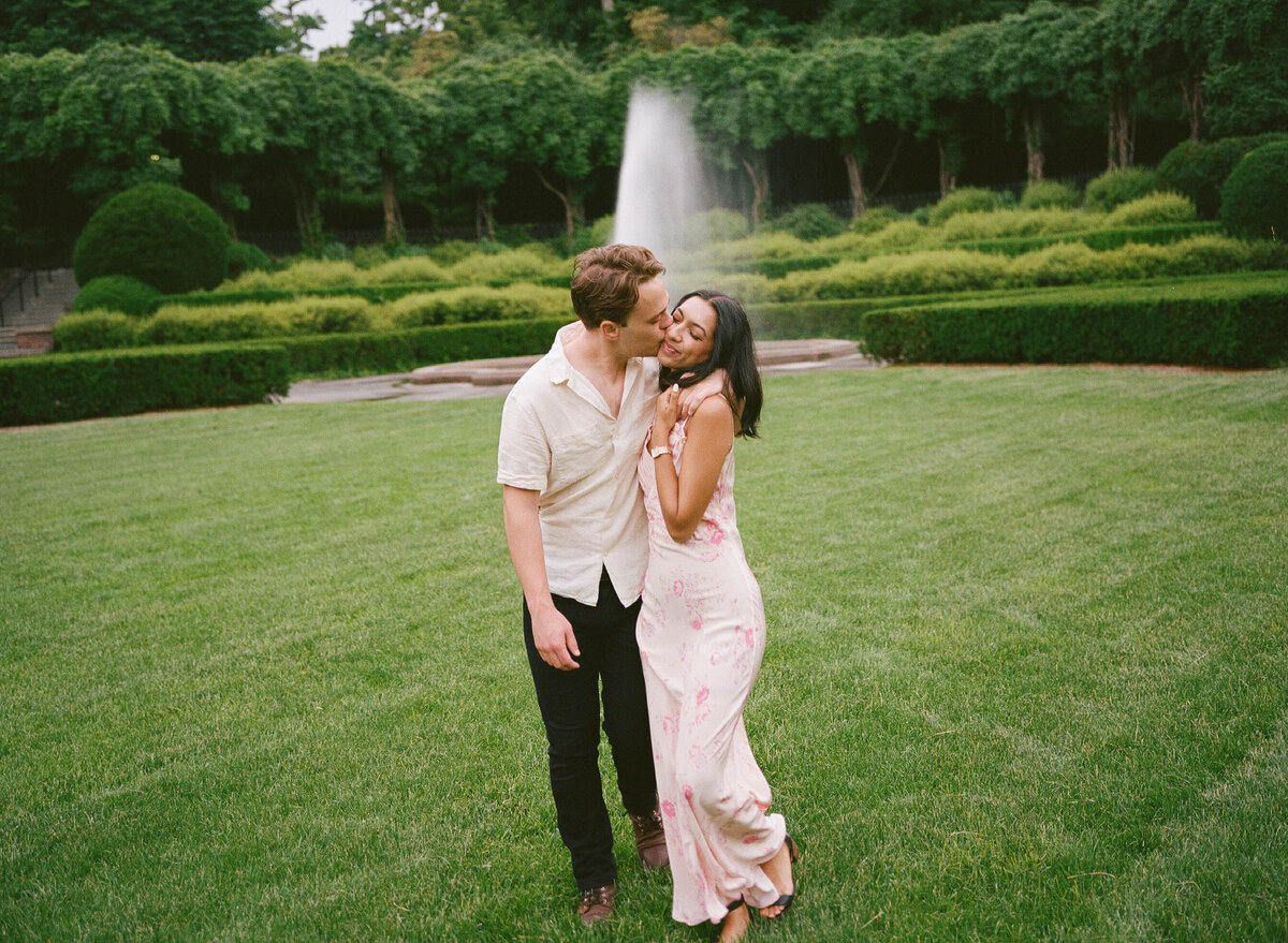 Couple standing in green manicured garden in front of a fountain