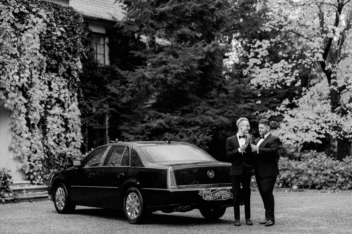 two grooms toasting champagne by just married car