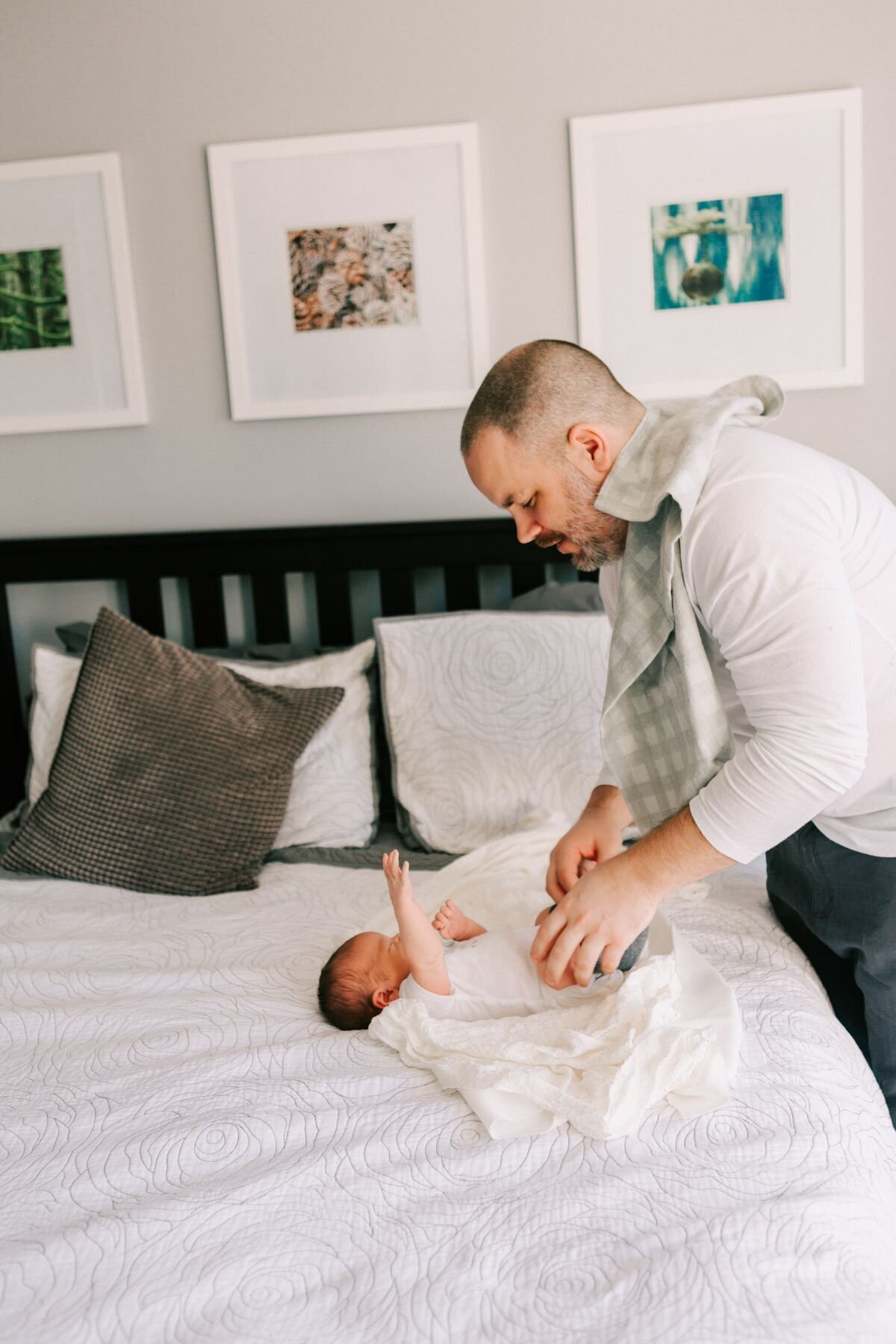 Dad removes baby from his swaddle on a white bed.
