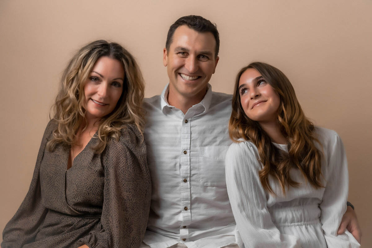 Father sits in the middle of mom and daughter as daughter looks up at dad