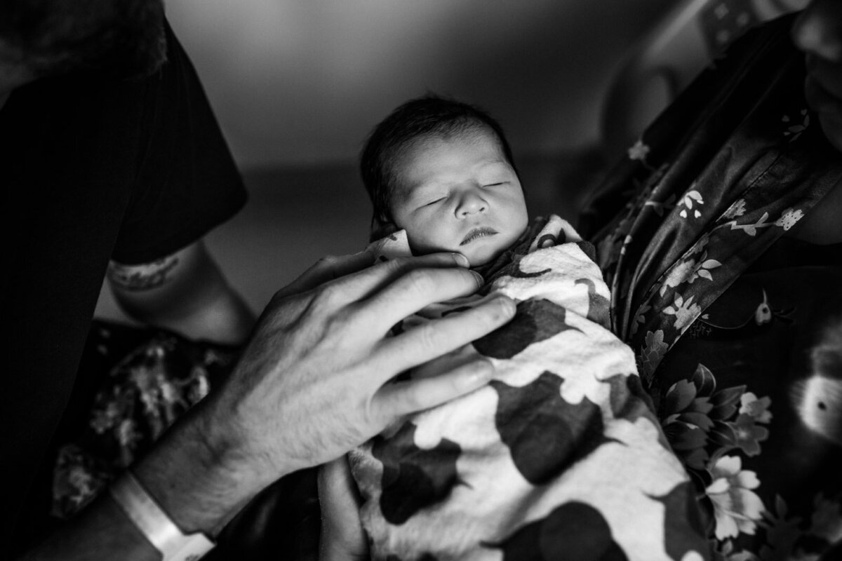 swaddled newborn sleeping in parents' arms in the hospital