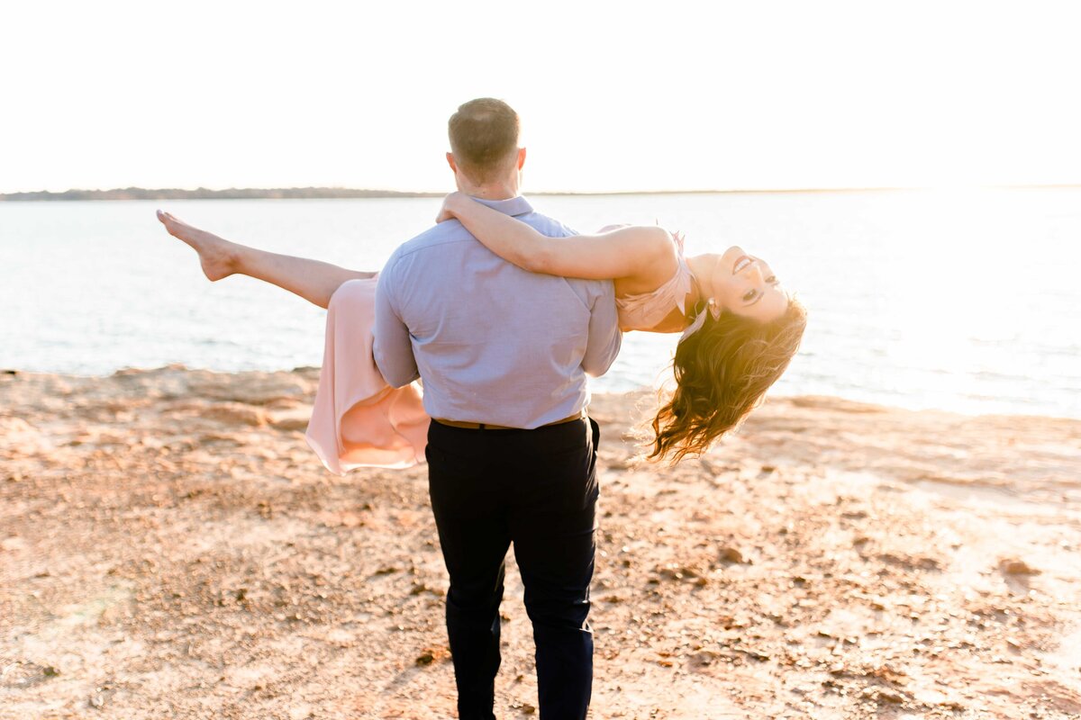 Happy Bride is lifted by her man and carried towards the lake as the sunsets.