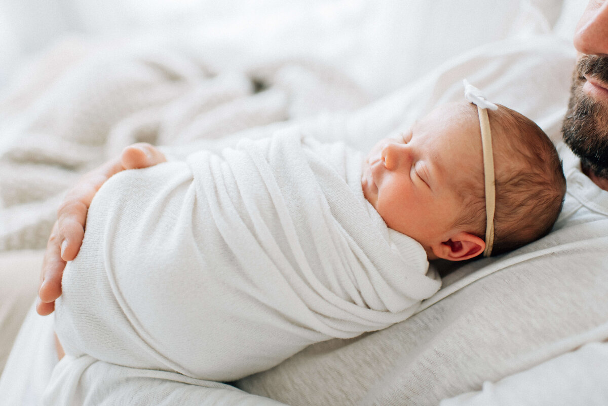 baby girl with bow swaddled asleep on dad's chest