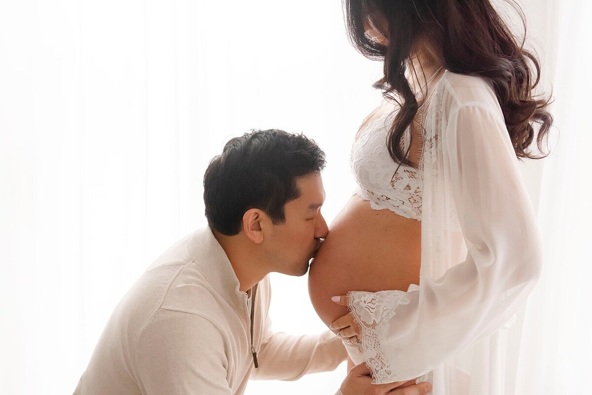 father to be kissing pregnant belly by maternity photographer in boston​