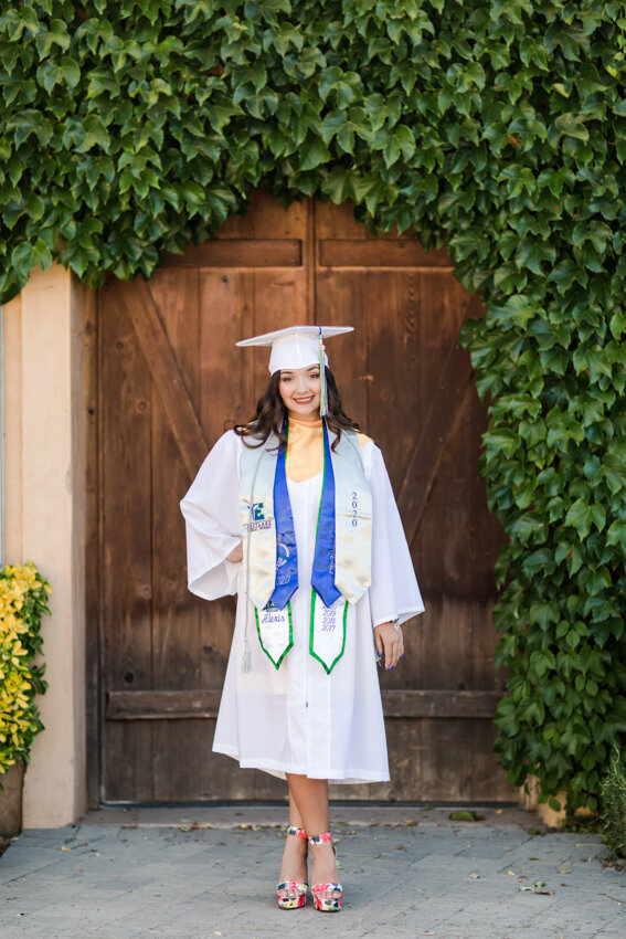 girl in cap and gown standing by ivy