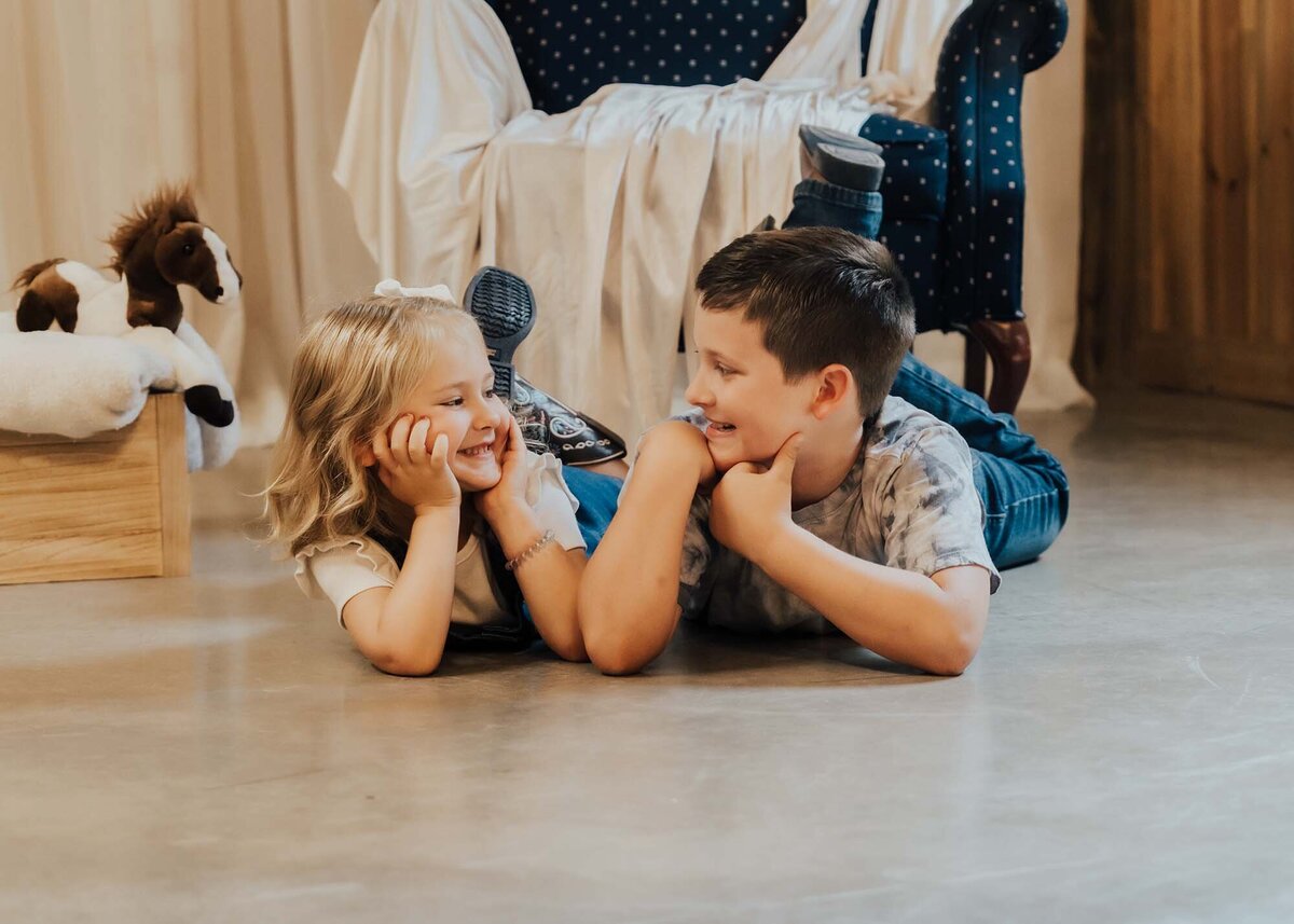 Maddie Rae Photography two little kids laying on their bellies on the ground looking at each other smiling