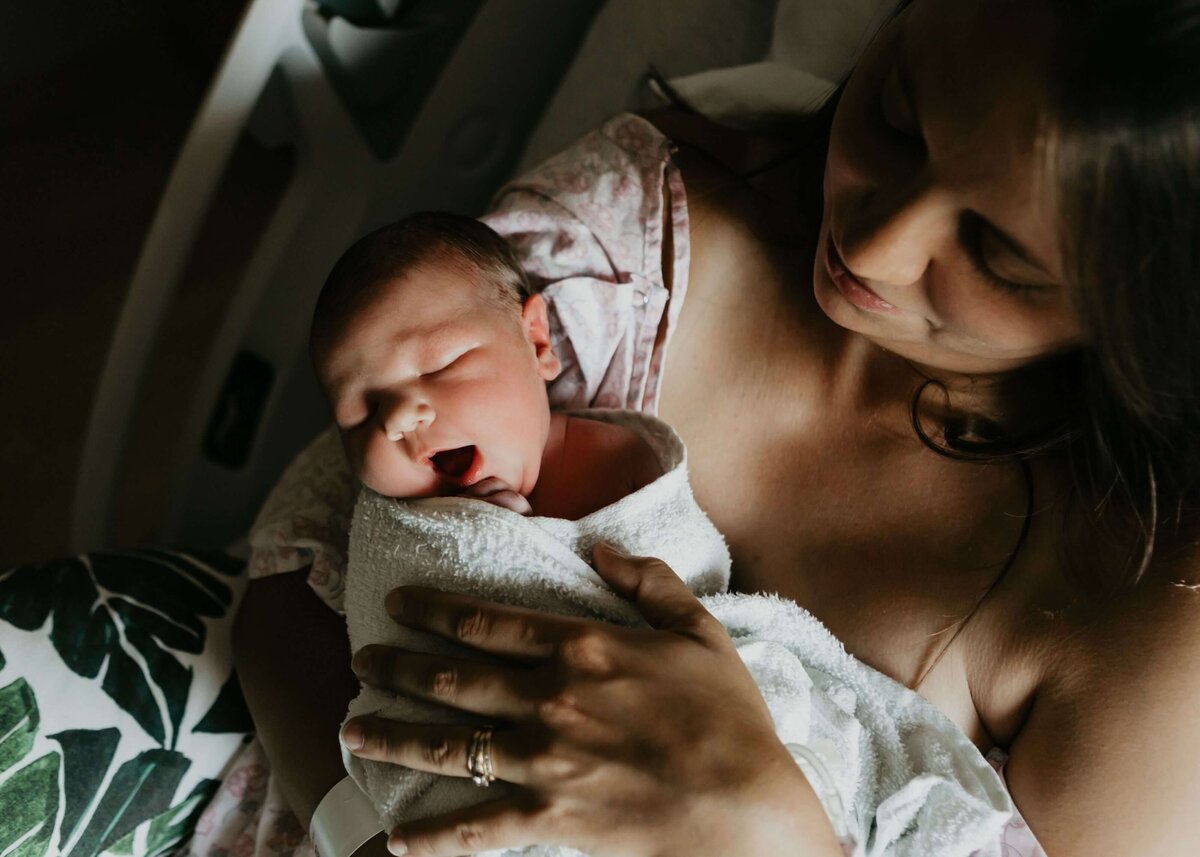 A woman holds her newborn baby in a hospital bed, captured by a Pittsburgh newborn photographer.