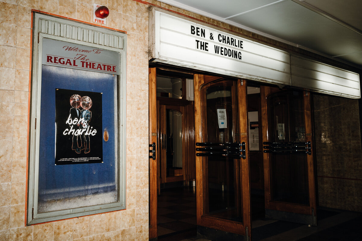 Outside the entrance of regal cinema, the ben and charlie wedding poster and theatre title above.