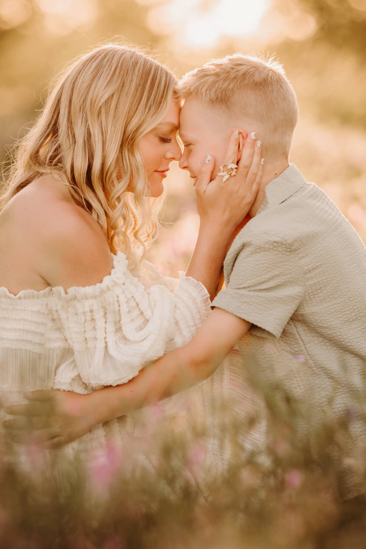 Mother and son touch foreheads while smiling at one another in a field. 
