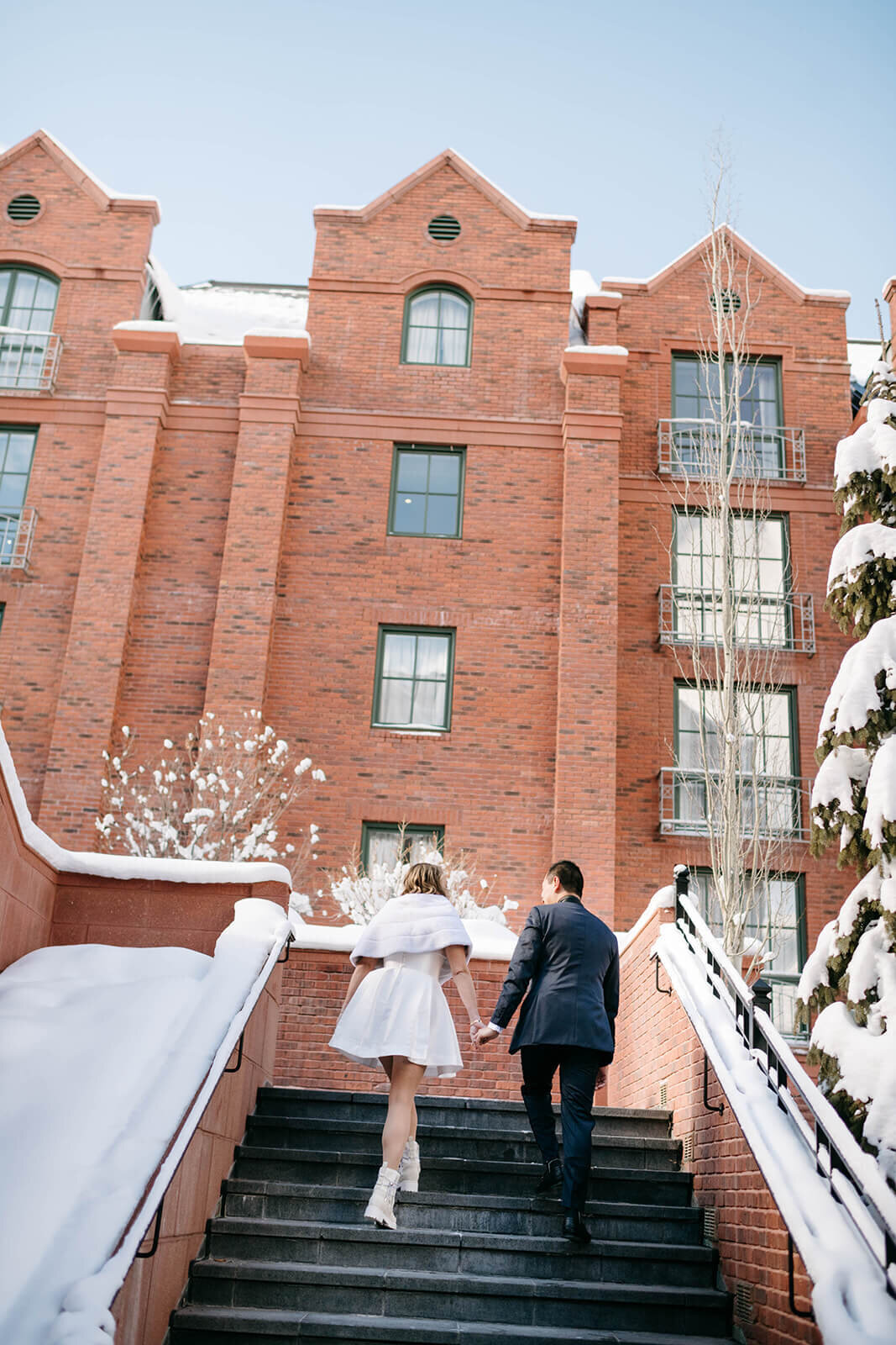 Bride and groom on the courtyard staircase at St. Regis Aspen, surrounded by elegant architecture and lush greenery.