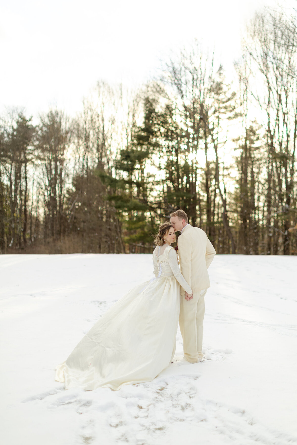 Husband kisses wife's forehead while they are holding hands with their eyes closed in the snow