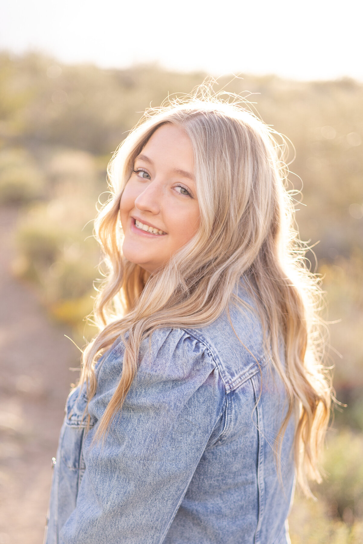 Senior girl smiles at camera with sunlit glow on her hair at Lake Pleasant in Peoria, AZ.
