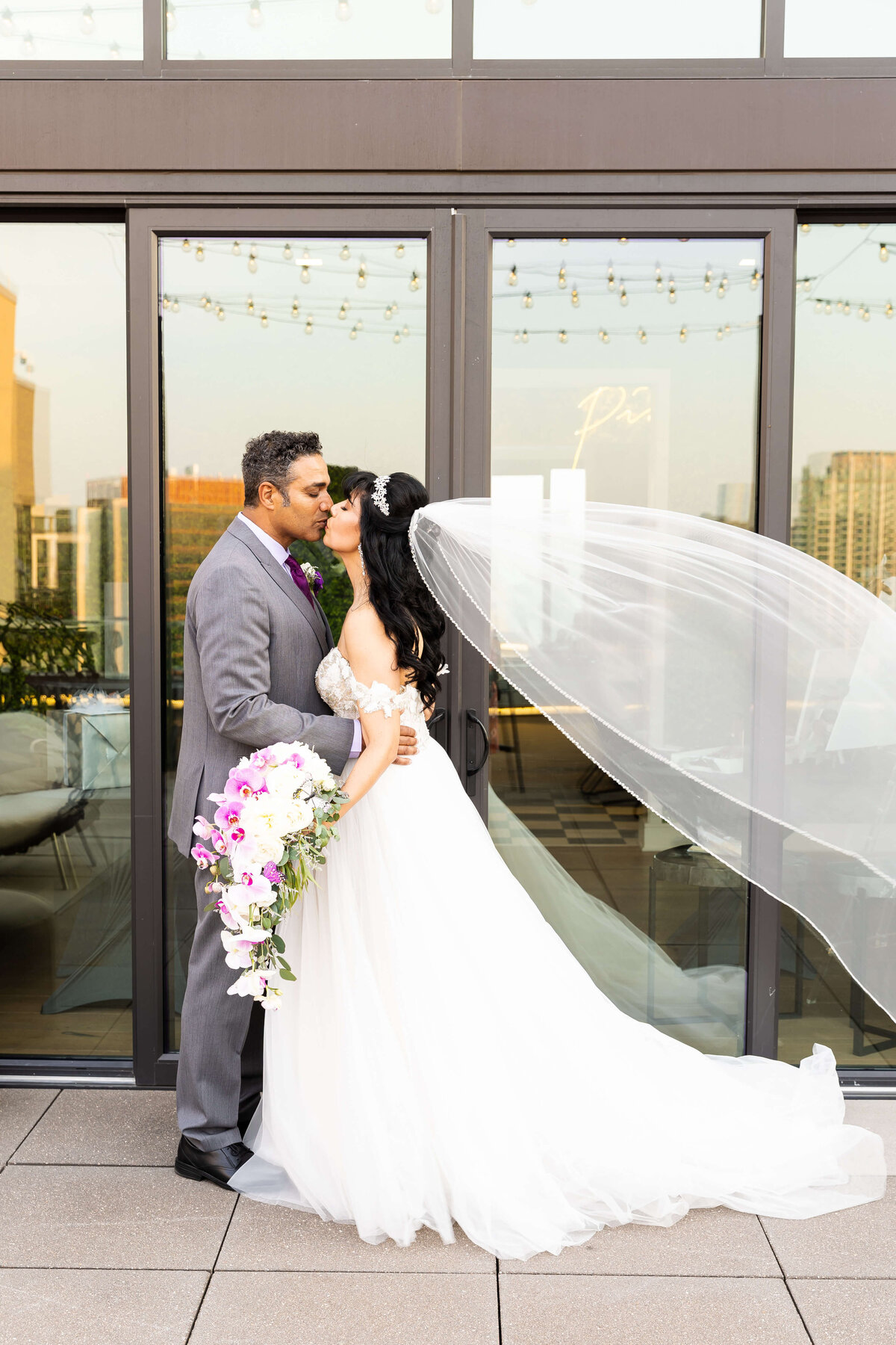 Bride and groom kissing as her veil blows in the wind on the rooftop of The Aertson hotel, Nashville