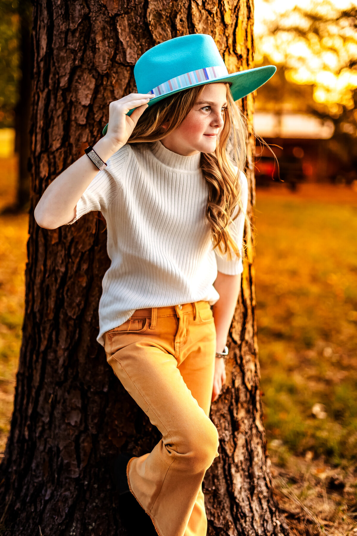 Girl leaning on a tree wearing vibrant colors at golden hour
