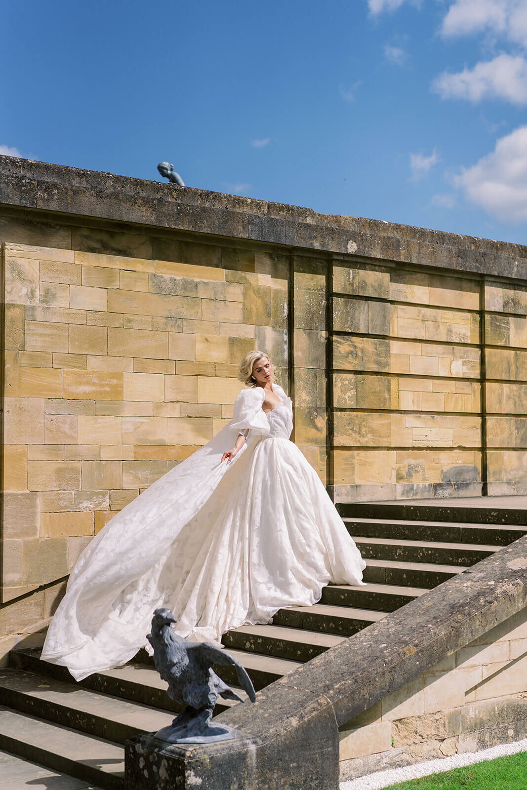 bride in a wedding gown walking up the stairs in the garden of blenheim palace as the wedding dress billows in the wind blowing behind the bride