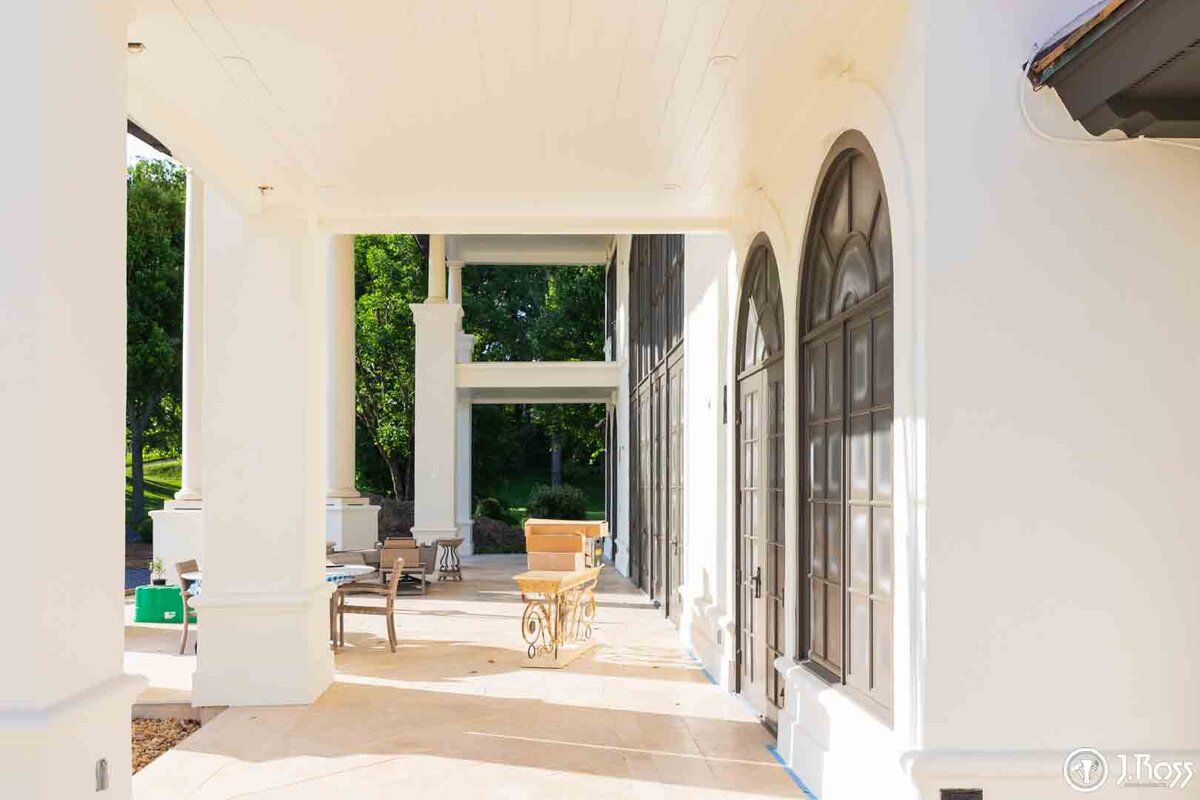 View down a newly painted white stucco and columned covered patio, contrasting the fresh finish with the dark-painted arched windows, a testament to high-quality home exterior painting Bristol, VA.