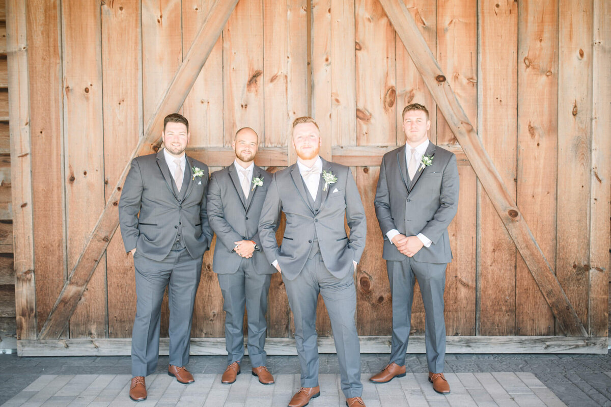 Groomsmen lined up infront of barn looking at Toronto wedding photographer