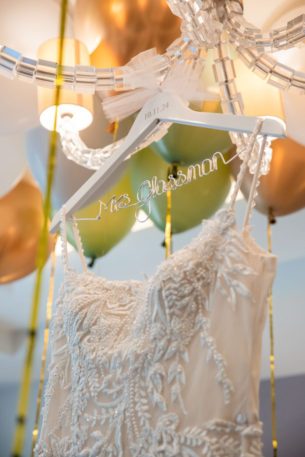 A wedding dress hangs on a hanger with the name mrs. glassman engraved on it