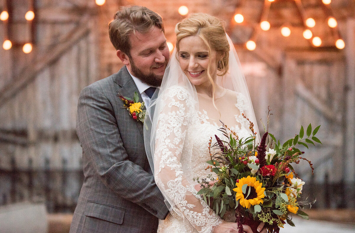 Groom embraces his bride holding a bouquet