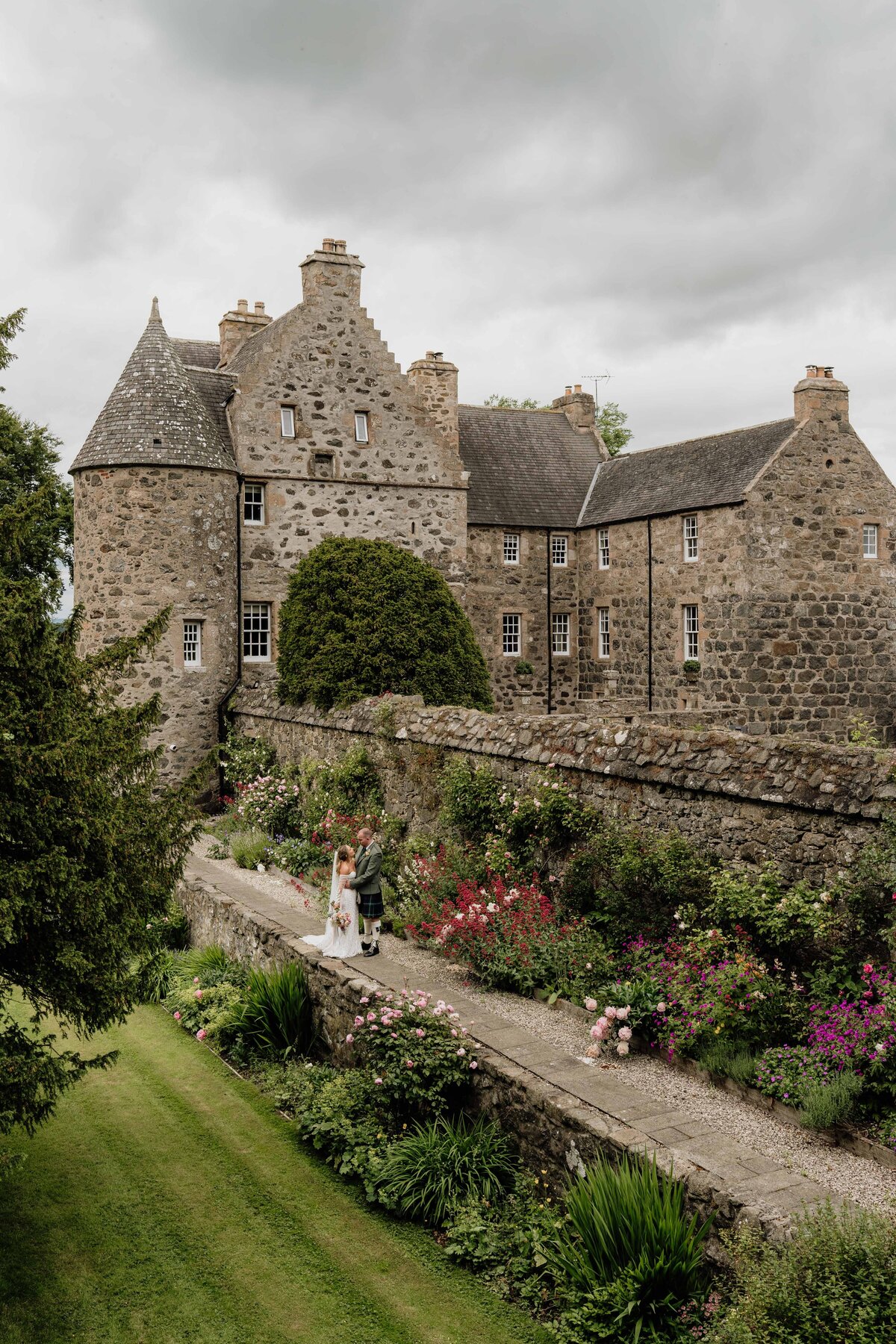 A very wide photograph of a bride and groom in the grounds of Barra Castle in Aberdeenshire.