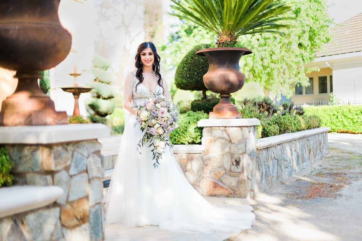 Bride looks at camera at Arden Hills on porch while holding a bouquet of flowers in Sacramento.
