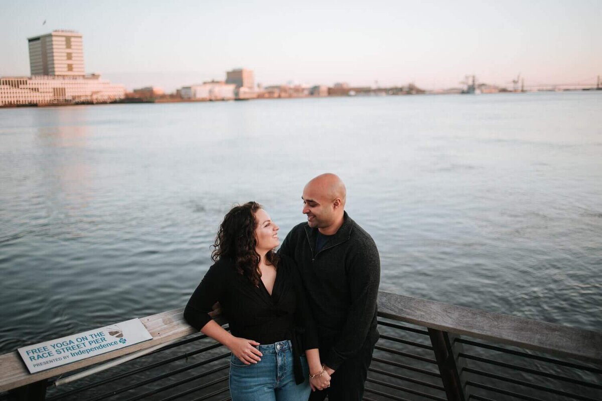 A soon-to-be wedded couple standing next to a bridge embracing each other in Philadelphia.