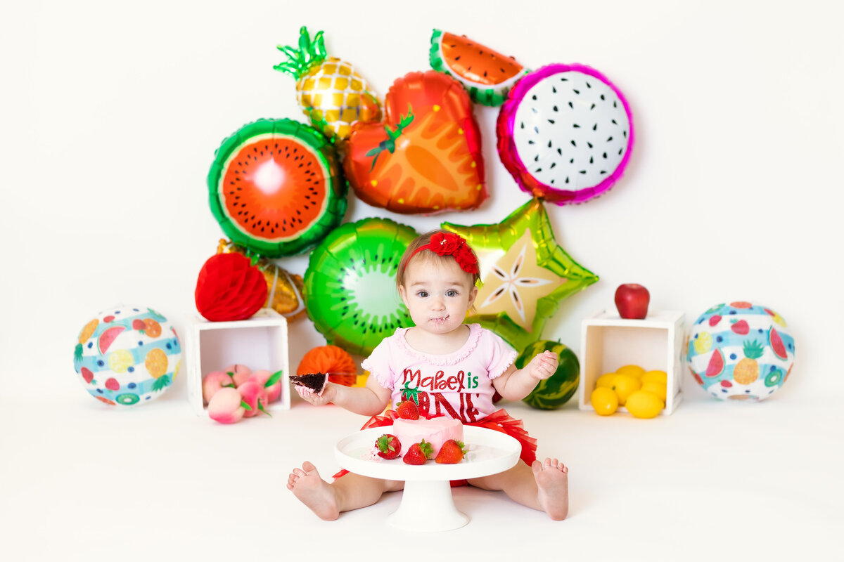 Cake Smash Photographer, a baby has a cake with strawberries and a fruit themed backdrop