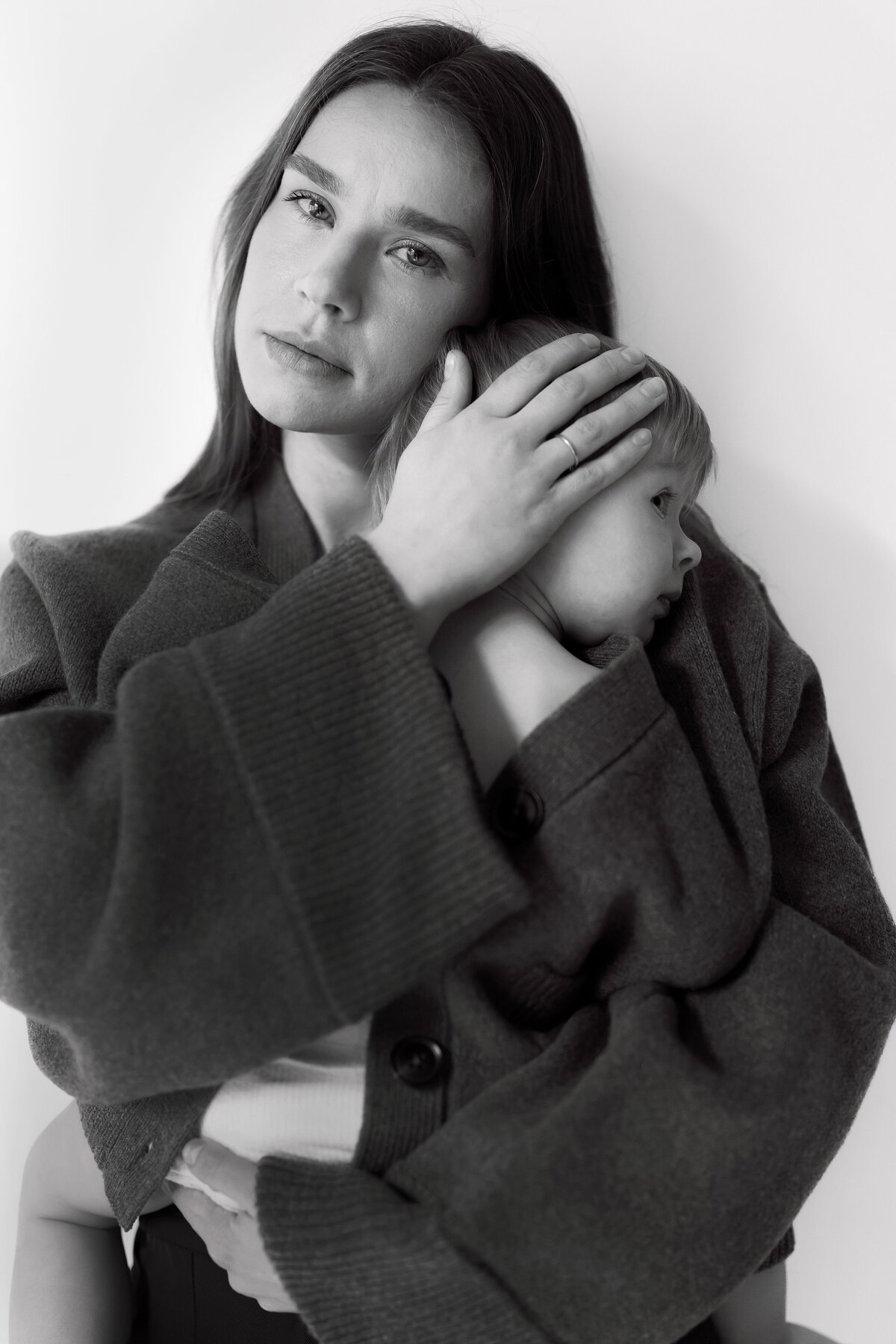Woman holds child in sweater while posing for camera in New york City photography studio.