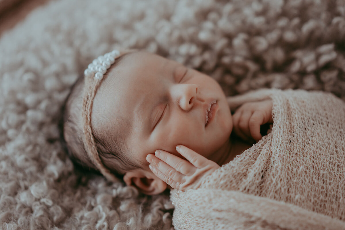 infant baby girl holds her face while in a swaddle