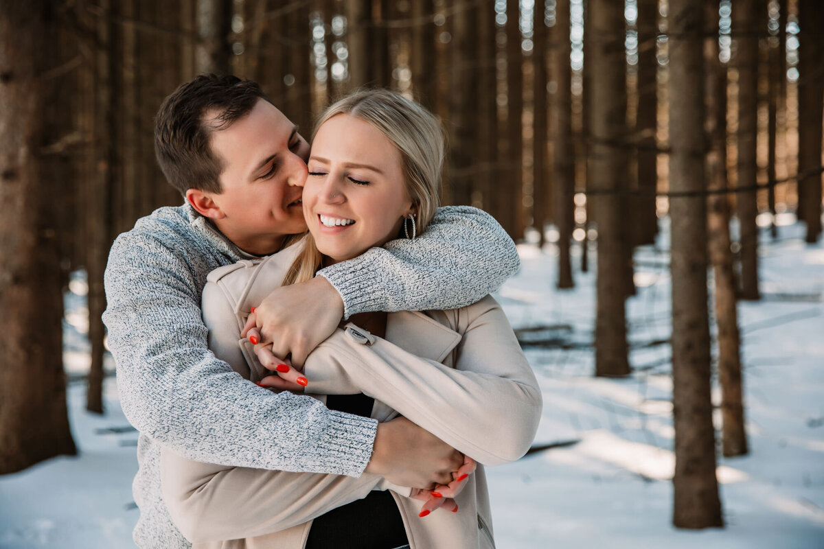 man wraps woman in giant hug from behind in a winter forest