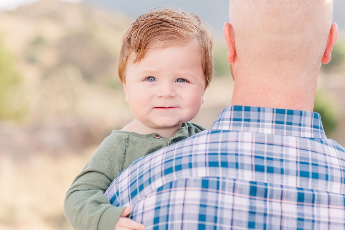 Baby boy looking over his dad's shoulder