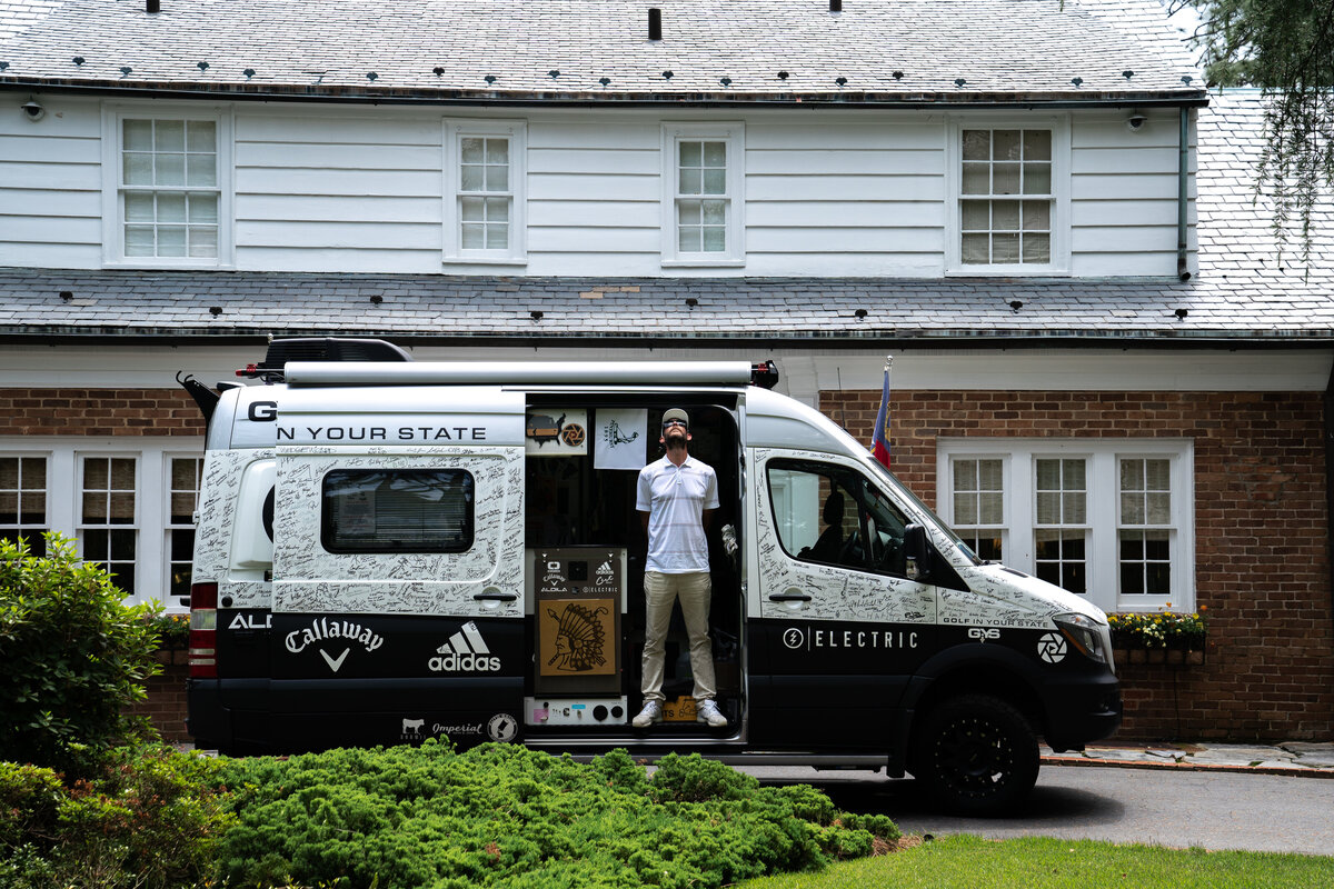 Custom Mercedes Camper parked in front of Dornoch Cottage in Pinehurst, NC with Golf In Your State influencer Matt Cardis looking up towards sky in door of camper. Taken in 2020.