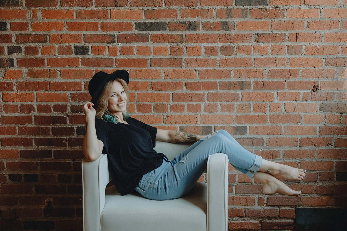 woman sits in chair in front of brick wall