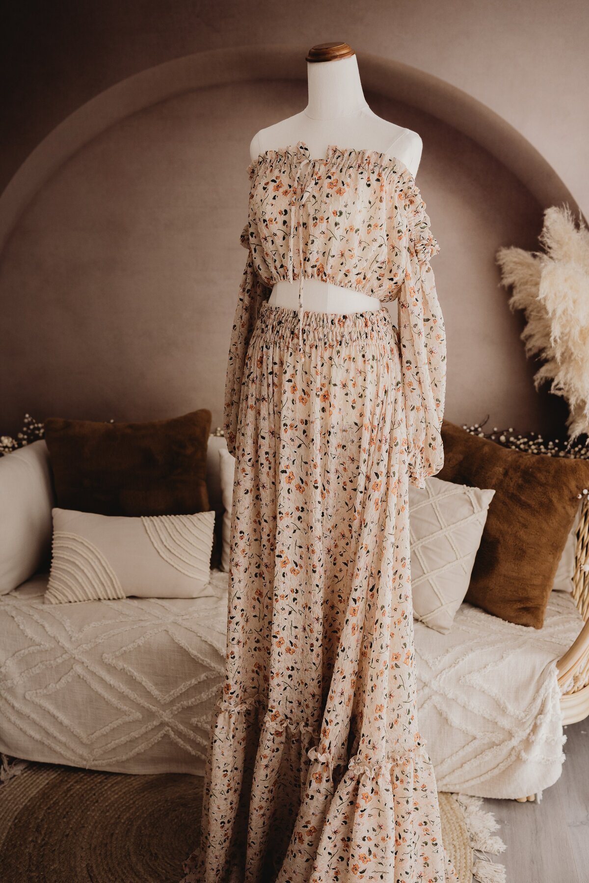 A floral off-shoulder, long-sleeve crop top and matching long skirt on a mannequin in a cozy, stylish room with a neutral color palette—perfect attire for elegant maternity photography sessions.