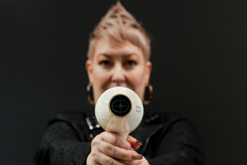 Hairstylist on a dark background with blow dryer pointed straight at camera