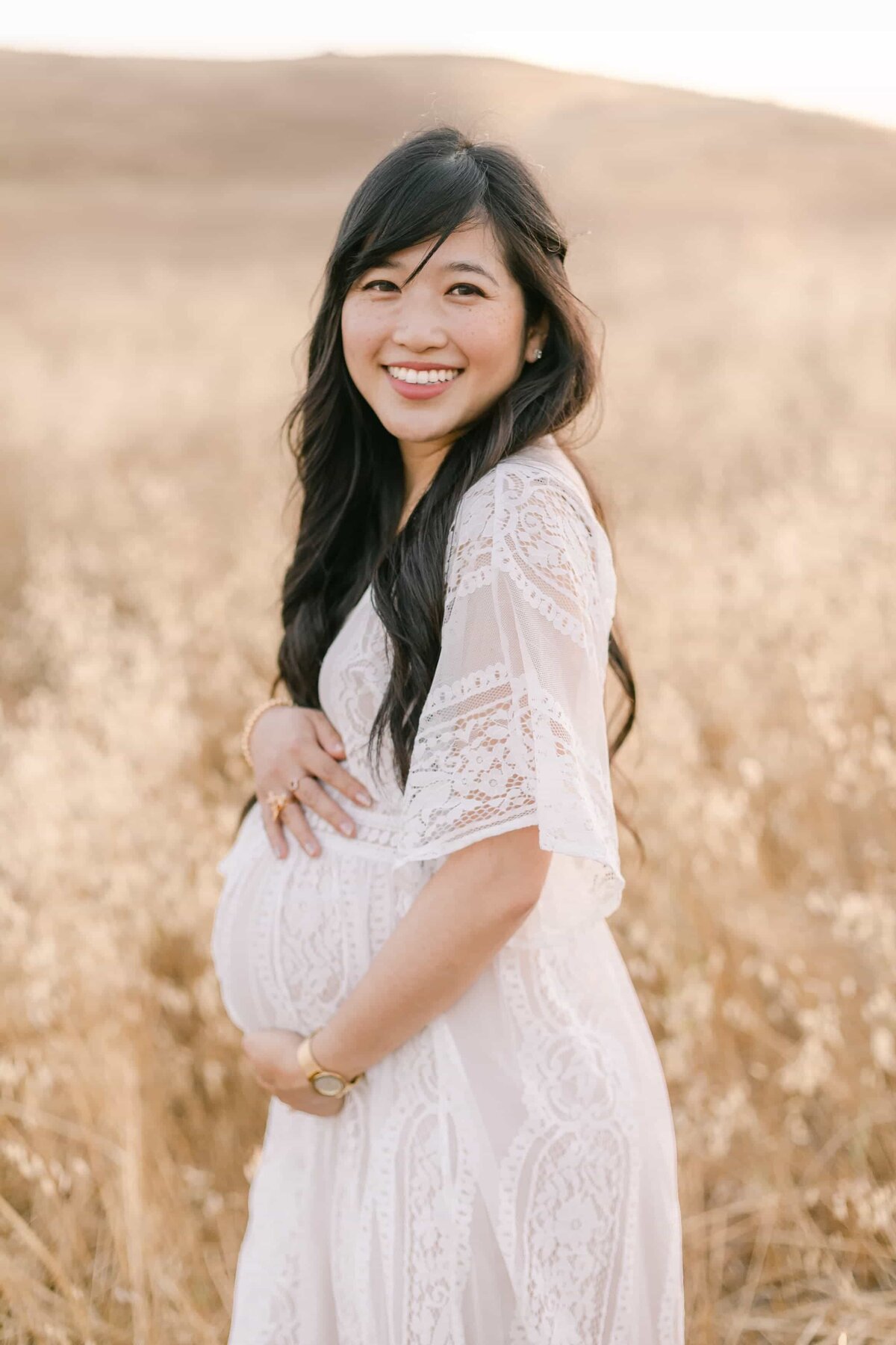 Orange County Maternity Photographer - pregnant woman smiling for camera while holding her baby bump