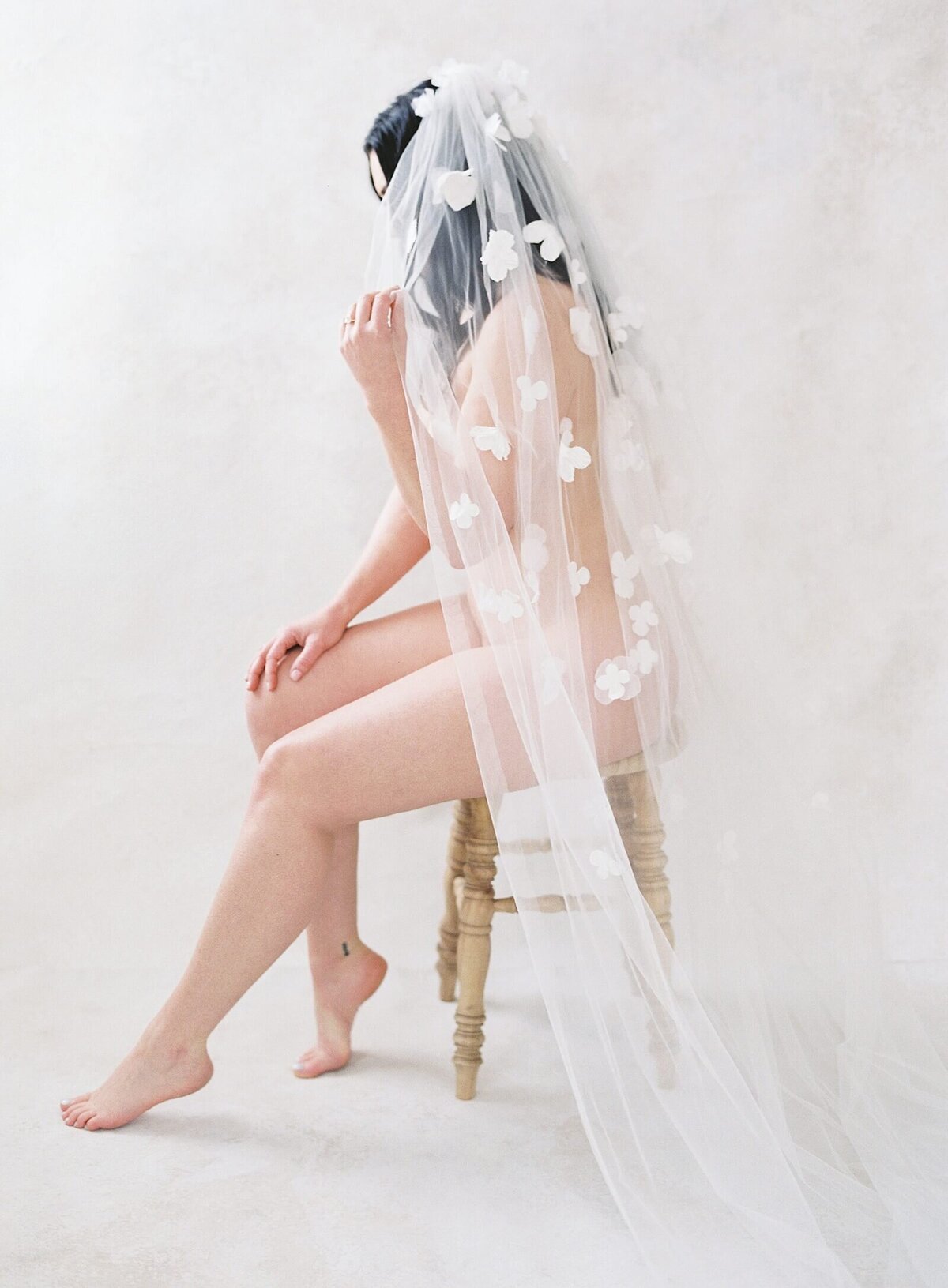 nude woman sits on a stool and holds onto a white floral applique veil photographed by seattle boudoir photographer Jacqueline Benét 