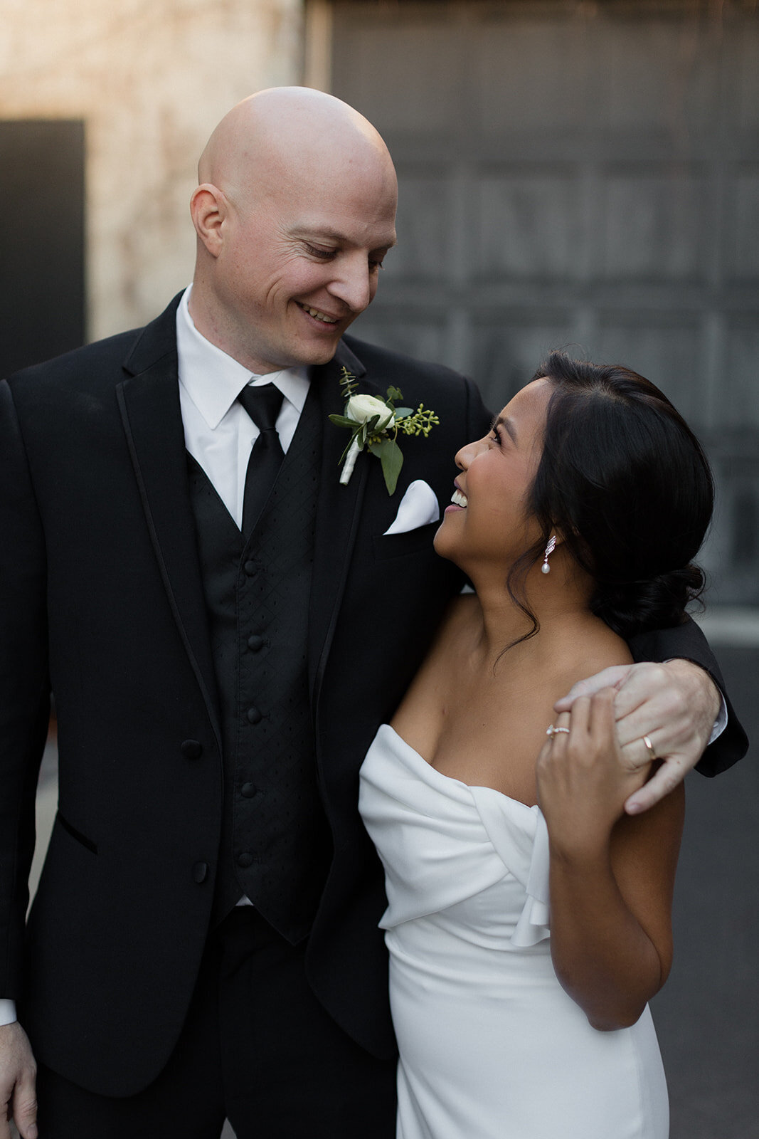 couple outdoors and grooms arm is around her shoulder and the look at each and smile