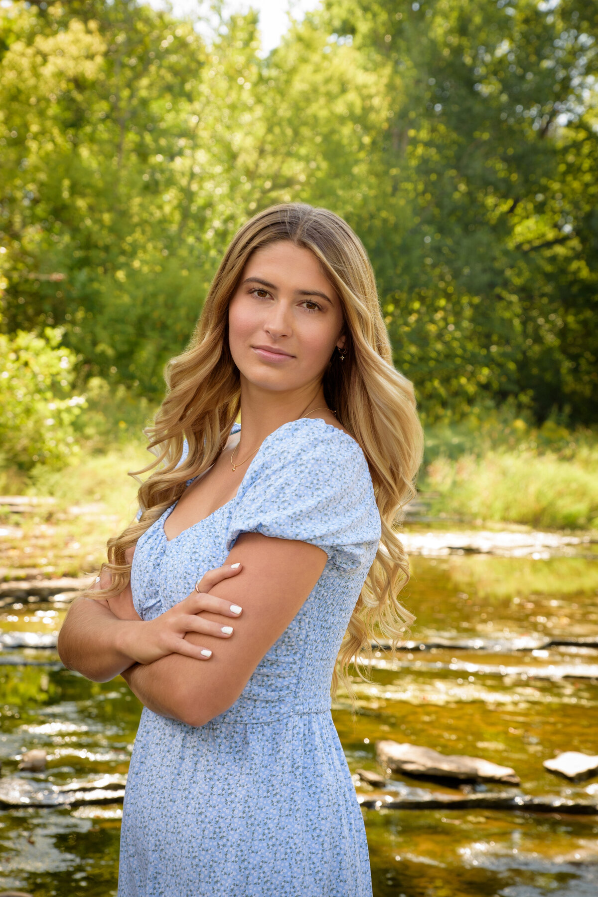 De Pere High School senior girl standing in creek wearing a light blue summer dress at Fonferek Glen County Park in Green Bay, Wisconsin